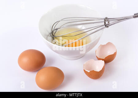 Kitchen wire whisk in bowl mixed egg and tow and broken eggs shell. Food and cooking concept Stock Photo