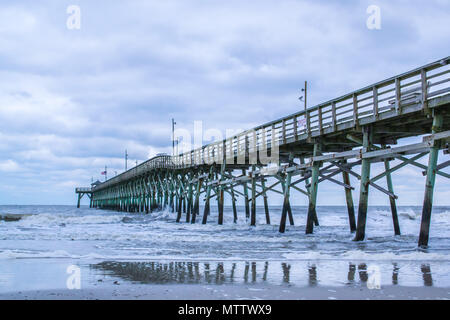 Under the Pier - beautiful ocean views from Oak Island beach, crashing waves, and the wooden pier on a cloudy day. Stock Photo