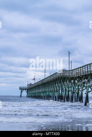 Under the Pier - beautiful ocean views from Oak Island beach, crashing waves, and the wooden pier on a cloudy day. Stock Photo