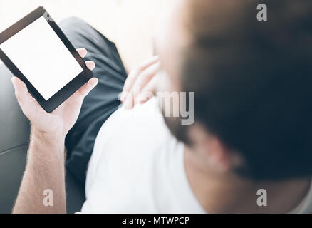 over the shoulder view of man sitting on armchair using e-book reader or tablet computer Stock Photo