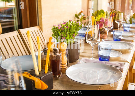 Light Table set for wedding or another catered event dinner. Wooden table served with plates, forks, spoons, glasses, napkins in the restaurant. Selec Stock Photo