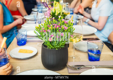 Dinning with family, friends. Blurred no face people enjoying meal while sitting at the dinning table with focus on the flower pot. Food Buffet Cateri Stock Photo