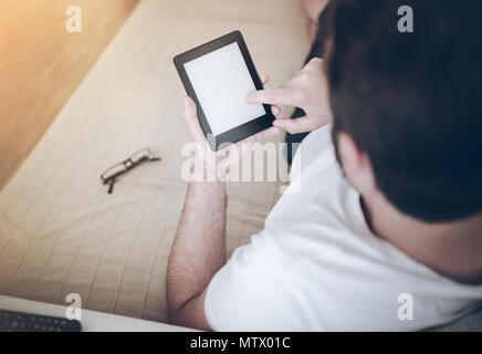 man relaxing on couch using e-book reader or tablet computer Stock Photo