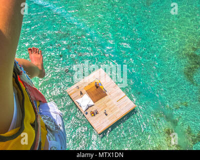 Aerial closeup view of a woman parasailing. Below, the landing platform on the spectacular blue sea of Deer Island, east coast of Mauritius, Indian Ocean. Stock Photo