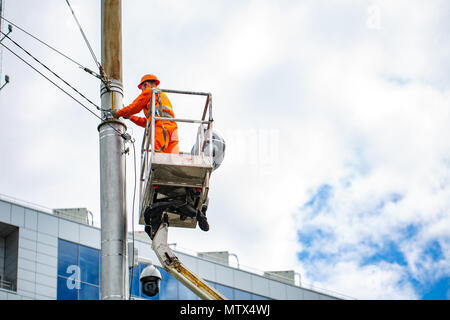 Electrician climbing work in the height on concrete electric power pole and basket with big crane on blue sky background Stock Photo