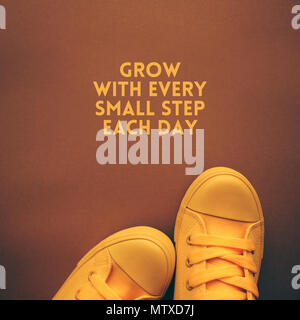 Grow with each small step every day motivational quote with young person in yellow sneakers standing above the text Stock Photo