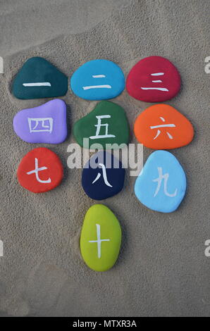 One to ten, chinese numbers painted over colored sea stones with sand background Stock Photo