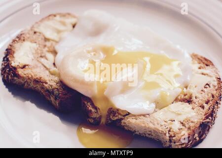 Runny poached egg on brown buttered toast - filter applied Stock Photo