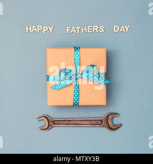 Happy Father's day card with gift box wrapped in kraft paper tied with blue ribbon in polka dots and wrench on blue grey background. Greeting card wit Stock Photo