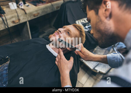 Male barber combing customers beard in barber shop Stock Photo