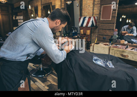 Male barber combing customers beard in barber shop Stock Photo