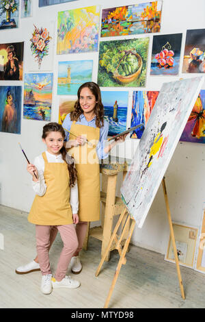 teacher and pupil standing near canvas on easel in workshop of art school Stock Photo