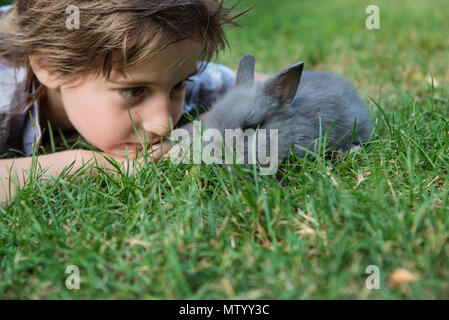 Boy lying on grass looking at a rabbit Stock Photo