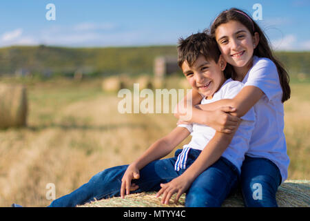 Girl sitting on a hay bale hugging her brother Stock Photo