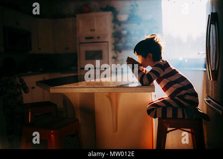 Boy sitting in kitchen eating his breakfast in morning light Stock Photo