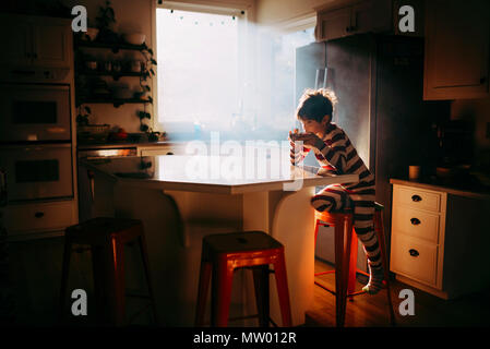 Boy sitting in kitchen eating his breakfast in morning light Stock Photo