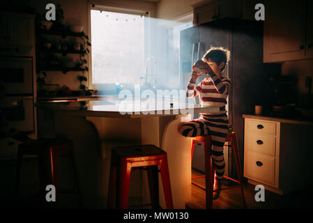 Boy standing in kitchen eating his breakfast in morning light Stock Photo