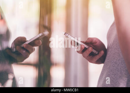 Using mobile phone in front of store shop window. Female hands holding smartphone device and using app to check the prices. Selective focus. Stock Photo