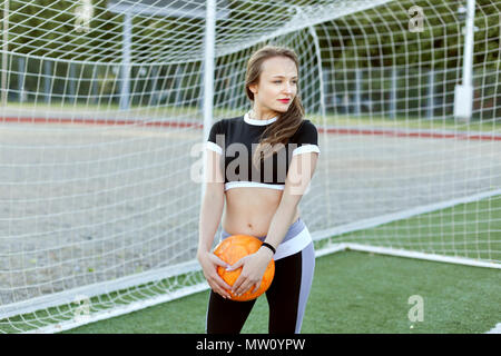 Young woman stands near a football goal and holds a ball in hand. Stock Photo