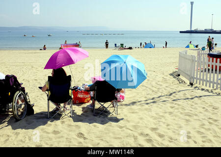 Weymouth, Dorset, UK. May 19, 2018. Holidaymakers enjoying relaxation on the beach under colorful parasols in the May sunshine at Weymouth in Dorset, 