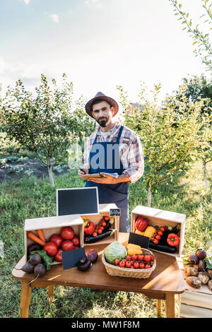 handsome bearded farmer selling organic vegetables and taking notes while standing at stall Stock Photo