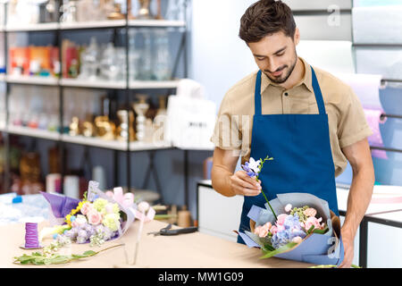 handsome young florist in apron arranging flowers while working in flower shop Stock Photo