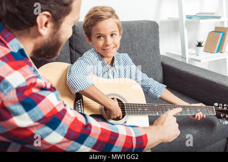 cropped shot of father teaching smiling little son playing guitar at home