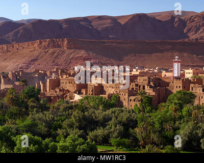 Clay fort of Tingir, the walls of orange-colored kazb on the background of orange mountains, the white tower of the mosque, the palm forest, Morocco. Stock Photo