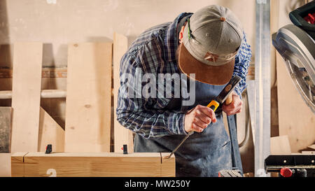 Close up experienced carpenter in work clothes and small buiness owner working in woodwork workshop,  using chisel for cutting out of wood  in worksho Stock Photo