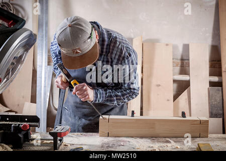 Close up experienced carpenter in work clothes and small buiness owner working in woodwork workshop,  using chisel for cutting out of wood  in worksho Stock Photo