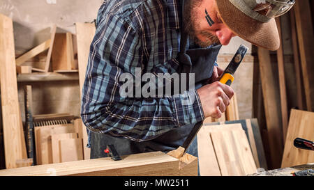 Close up experienced carpenter in work clothes and small buiness owner working in woodwork workshop,  using chisel for cutting out of wood  in worksho Stock Photo