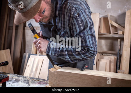 Close up experienced carpenter in work clothes and small buiness owner working in woodwork workshop,  using chisel for cutting out of wood  in worksho Stock Photo