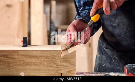 Close up experienced carpenter in work clothes and small buiness owner working in woodwork workshop,  using chisel for cutting out of wood  in worksho Stock Photo