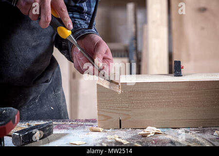 Close up experienced carpenter in work clothes and small buiness owner working in woodwork workshop,  using chisel for cutting out of wood  in worksho Stock Photo