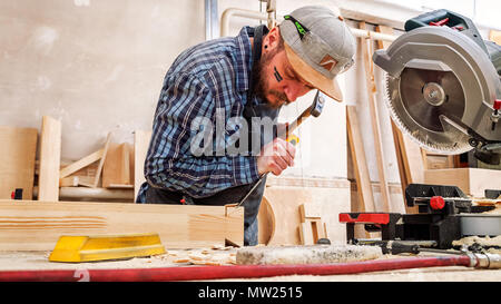 Close up experienced carpenter in work clothes and small buiness owner working in woodwork workshop,  using chisel for cutting out of wood  in worksho Stock Photo