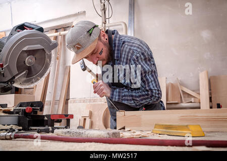 Close up experienced carpenter in work clothes and small buiness owner working in woodwork workshop,  using chisel for cutting out of wood  in worksho Stock Photo
