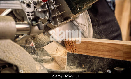 Close up of experienced carpenter in work clothes and small buiness owner working in woodwork workshop, using a circular saw to cut through a wooden p Stock Photo