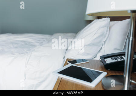 smartphone and tablet on bedside table in hotel room Stock Photo