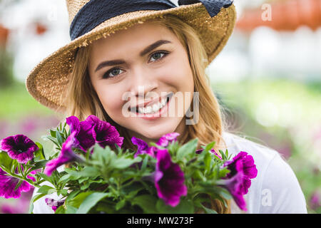 Blonde woman holding purple flowers in glasshouse Stock Photo