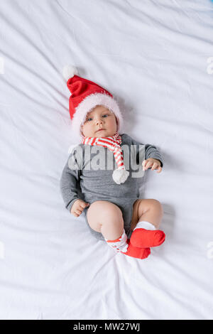 overhead view of adorable infant boy in santa claus hat lying on bed Stock Photo
