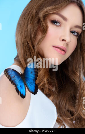 attractive young woman with butterfly on shoulder isolated on blue Stock Photo