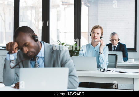 three multiethnic business people in headsets working with laptops in modern office Stock Photo
