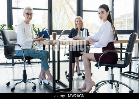three professional businesswomen sitting at table and looking at camera Stock Photo