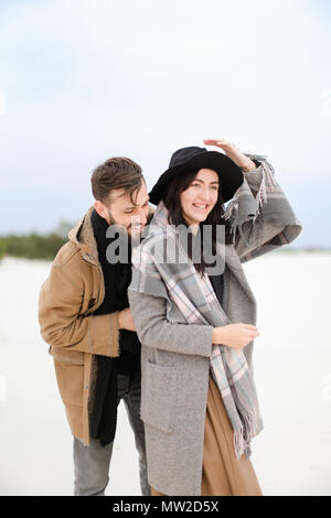 Smiling female person and man with beard wearing coats and scarfs standing in winter snow background. Stock Photo
