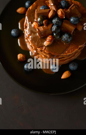 Stack of chocolate pancakes with icing, blueberry, almond, hazelnut and pieces of chocolate. Selective focus. Stock Photo