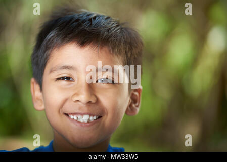 Smiling with teeth hispanic boy headshot on blurred summer background Stock Photo