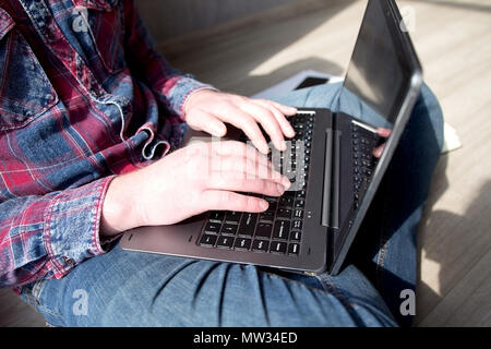Cropped shot of a mans hands typing on a laptop covered in sun. Man working on computer typing sitting on wood floor in his apartment. Stock Photo