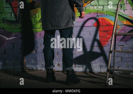 low section of street artist painting graffiti on wall at night Stock Photo