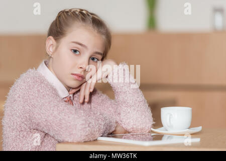 bored kid sitting at table with digital tablet and looking at camera Stock Photo