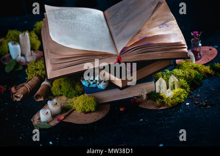 Open book with candles, crystals, and moss. Reading fantasy concept with copy space. Magical still life on a dark background with occult equipment. Stock Photo